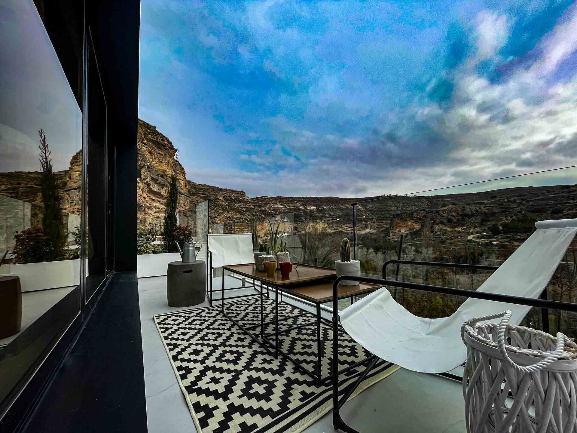 Un balcón con vistas a un paisaje rocoso, una alfombra estampada y una mesa con sillas.