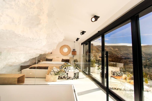 A modern bedroom with a large window, a bed, and a view of the outdoors. - KAHF Cave Suite (Grotte Lomas de Ruvira Hotel) (Jorquera)