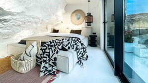 Un dormitorio con una cama grande, vistas al exterior a través de una puerta de vidrio y una pared con textura.