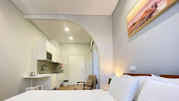 Habitación de hotel con cama, silla, escritorio y kitchenette.