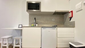 Cocina compacta con armarios blancos, microondas integrado, lavavajillas y un cubo de basura.