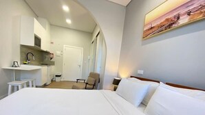 Una habitación de hotel con cama, una silla, un escritorio y un kitchenette.
