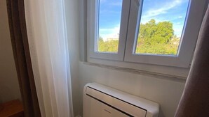 A room with a window, a white radiator, and a wooden floor. - Canto Doce Portela - C (Setúbal)