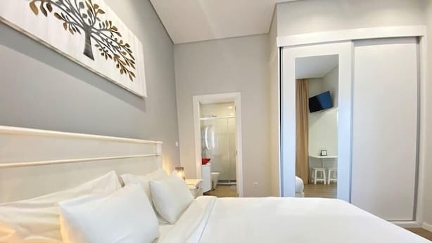 A hotel room with a large bed, a wardrobe, a TV, and a bathroom visible through an open door. - Canto Doce Portela - C (Setúbal)