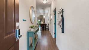 Un pasillo con puerta de madera, una consola con planta, un espejo y un perchero.