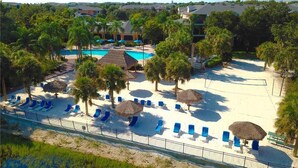 Un resort con piscina, zona de playa con sillas y sombrillas, y palmeras.