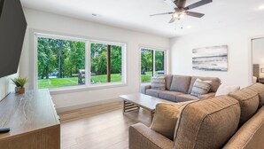 Ein modernes Wohnzimmer mit großem Fenster, Deckenventilator und Couchtisch aus Holz.