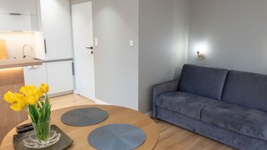 Uma sala de estar moderna com um sofá cinzento, uma mesa de centro de madeira com dois suportes azuis para copos e um vaso com flores amarelas.