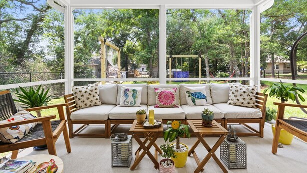 A covered outdoor seating area with a sofa, chairs, and tables, surrounded by potted plants and a view of a playground. - Awesome New, Dog-Friendly, Spacious Beach Home - Oak Island NC - Steps to ocean (Oak Island)