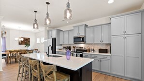 A modern kitchen with grey cabinets, a central island, bar stools, and pendant lighting. - Awesome New, Dog-Friendly, Spacious Beach Home - Oak Island NC - Steps to ocean (Oak Island)