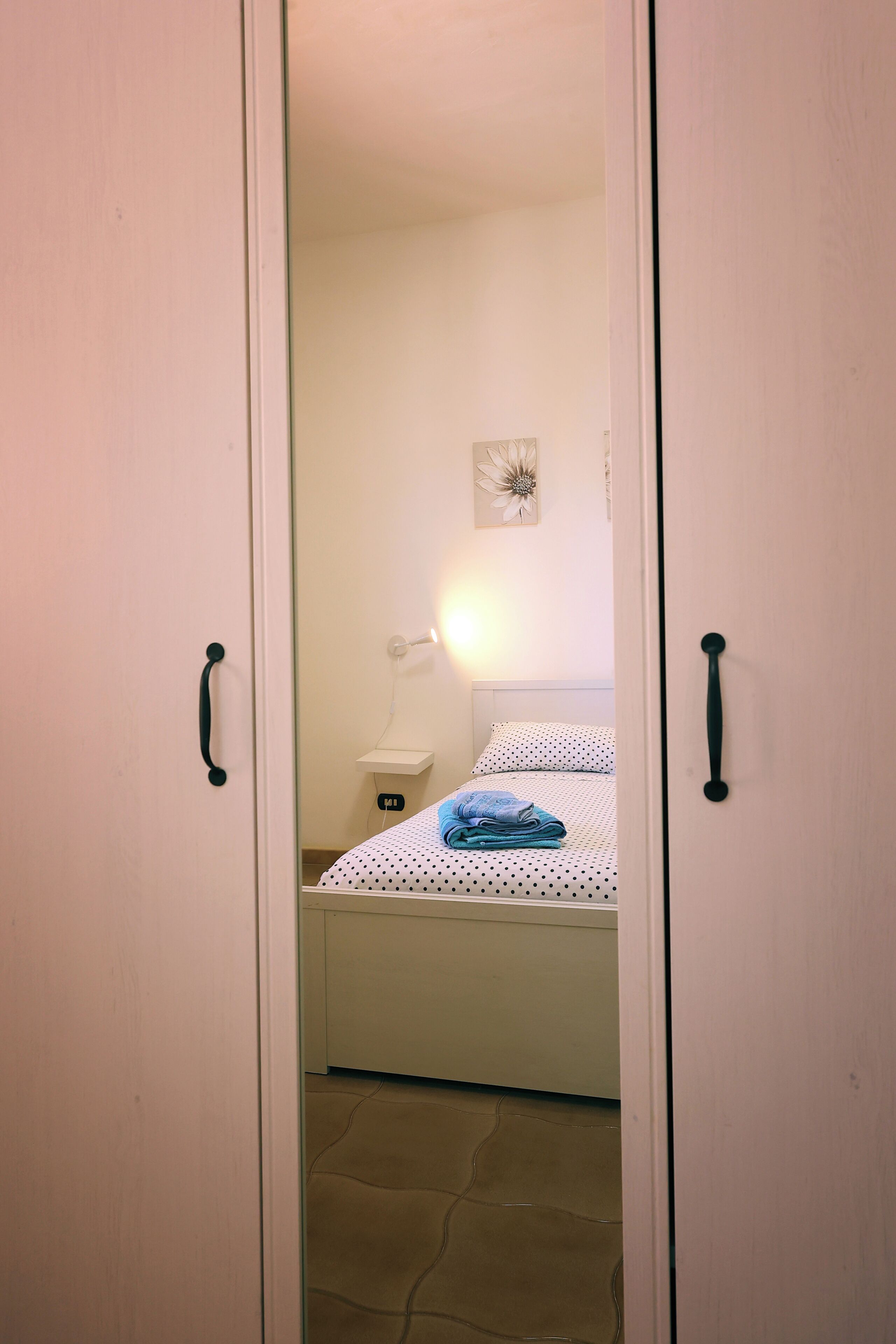 A bedroom with a bed, a nightstand, and a wall-mounted lamp.