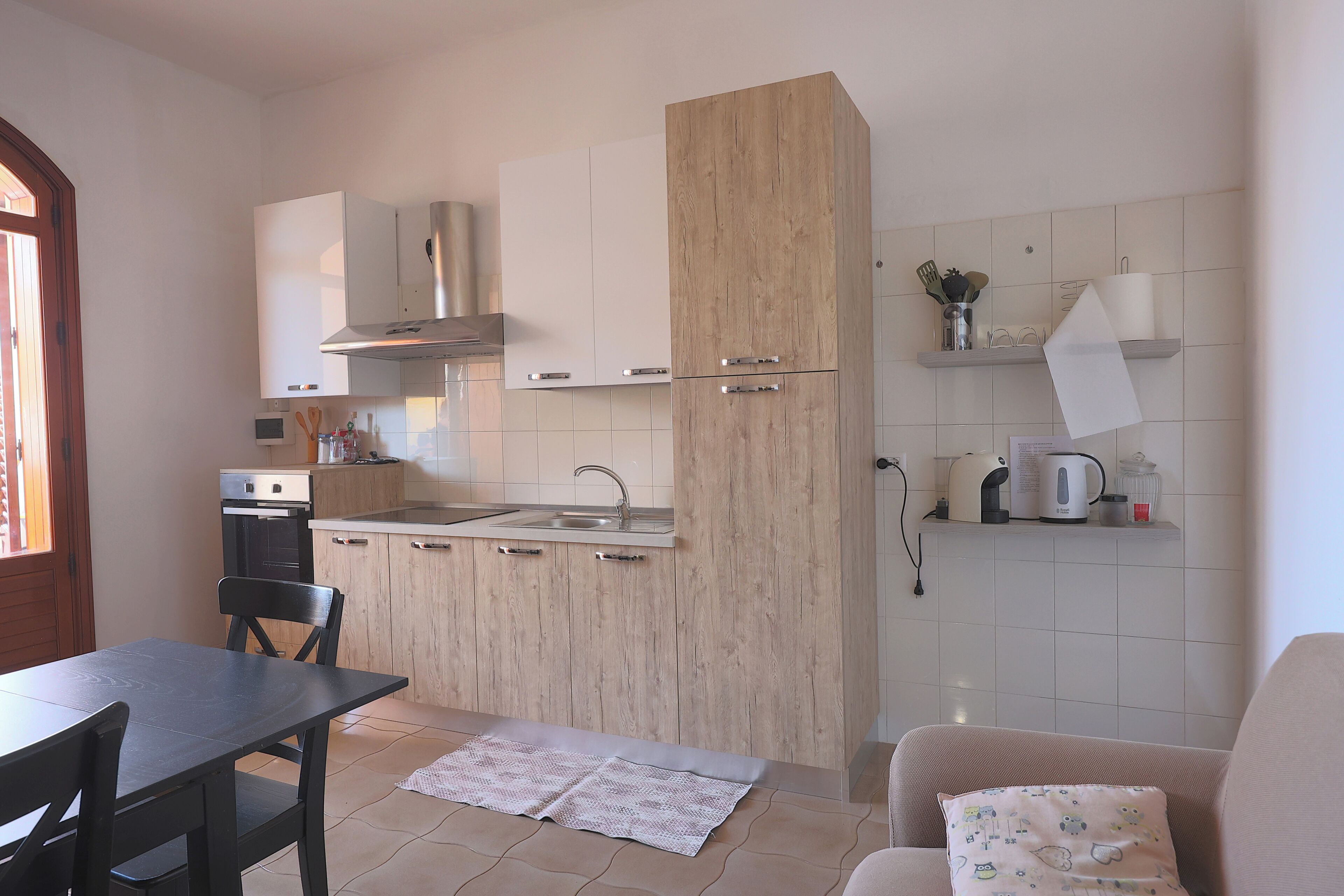 Een kleine keuken met een eethoek, met daarin een kookplaat, oven, spoelbak en houten kastjes.