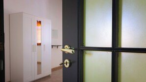 Una habitación con una puerta negra, un armario blanco y una ventana con persianas.