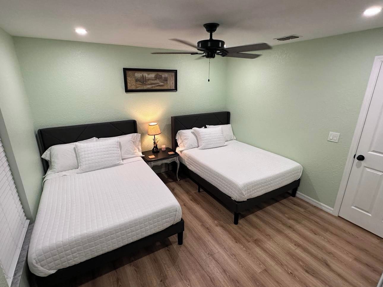 A bedroom with two beds, a ceiling fan, and a nightstand with a lamp.