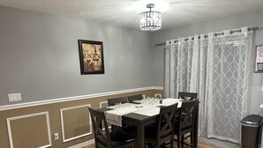 A dining area with a round table, six chairs, a chandelier, a framed picture on the wall, and a trash bin. - King Bed, Clean & Cozy, 10 Min to WEC Ocala (Ocala)