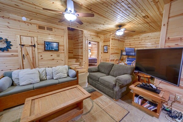 L’intérieur d’un chalet en bois, avec un canapé, un divan, une table basse, un téléviseur et une bibliothèque.