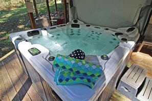 Un bain à remous avec un couvercle, un tapis de bain à pois et une petite table avec une tasse.