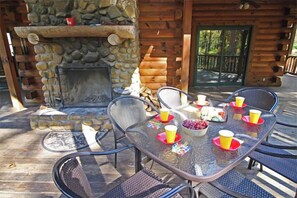 Un espace de restauration en plein air doté d’une cheminée en pierre, de chaises en métal et d’une table dressée avec des tasses et un saladier rempli de fruits.
