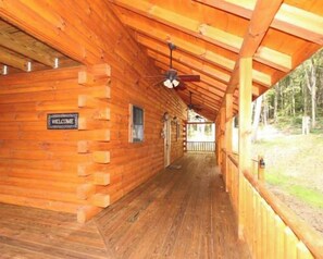 Une cabane en bois avec un porche couvert, une pancarte de bienvenue et un ventilateur de plafond.
