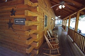 Eine Holzhütte mit einem 'WELCOME'-Schild, Schaukelstühlen und einer Veranda.