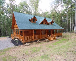 Une cabane en rondins avec un porche, une cheminée et une porte d’entrée.