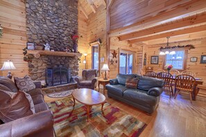 L’intérieur d’un chalet confortable, avec une cheminée en pierre, des canapés en cuir, un coin repas et des murs en bois.