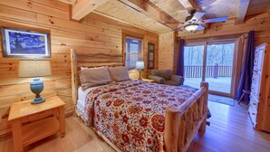 Ein Schlafzimmer einer Holzhütte mit einem Bett, einem Nachttisch, einem Deckenventilator und einem großen Fenster.
