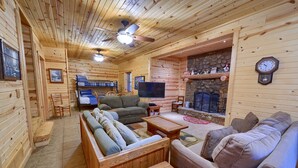 Ein gemütliches Blockhaus-Interieur mit Holzwänden, einem Steinkamin, einem Fernseher und bequemen Sitzgelegenheiten.