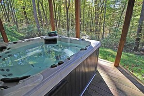 Un bain à remous sur une terrasse en bois, entouré d’une forêt.