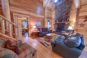 L’intérieur d’un chalet accueillant, avec une cheminée en pierre, des murs en bois, un canapé, une table basse et un escalier.