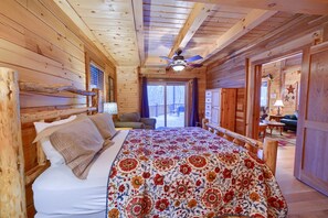 Ein Schlafzimmer in einer Holzhütte mit Bett, Deckenventilator und Blick ins Freie.