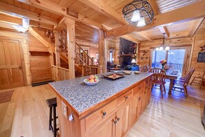 Ein Holzblockhaus-Interieur mit Kücheninsel, einer Holztreppe und einem Kamin aus Stein.