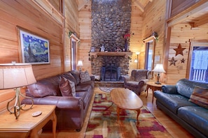 Ein gemütliches Blockhaus-Interieur mit Kamin, Ledersofas und einem farbenfrohen Teppich.