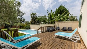 Une terrasse en bois avec une piscine, des chaises longues et un petit espace patio comprenant une table et des chaises.