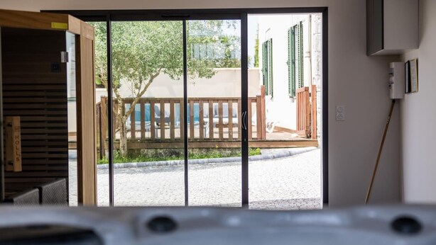 On aperçoit, à travers une porte-fenêtre coulissante, une cour intérieure avec une clôture en bois, un banc et un petit jardin.