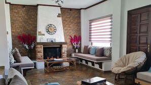 A cozy living room with a fireplace, comfortable seating, and a stone floor. - Romantic traditional Villa with huge garden, swimming pool, basketball court etc (Avlonas)