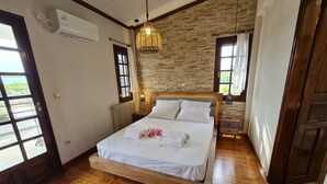 A bedroom with a stone wall, a wooden bed, and a hanging light fixture. - Romantic traditional Villa with huge garden, swimming pool, basketball court etc (Avlonas)