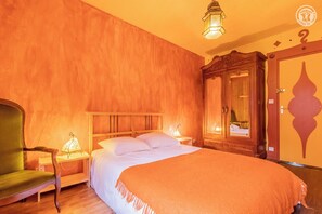Een hotelkamer met een bed, een houten garderobe, een groene fauteuil en een nachtkastje met een lamp.