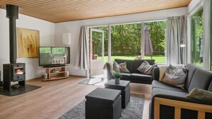 Ett modernt vardagsrum med en öppen spis, en soffa, ett soffbord och stora fönster som ger utsikt över omgivningen.