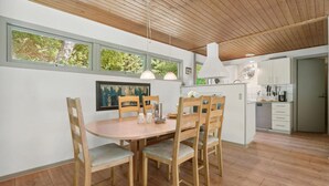 En matplats med ett träbord och stolar, en tavla på väggen och ett kök i bakgrunden.