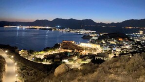 Un pueblo costero de noche con vista al mar y montañas al fondo.