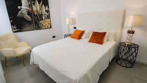 Habitación de hotel con una cama grande, dos mesitas de noche, una silla y una obra de arte en la pared.