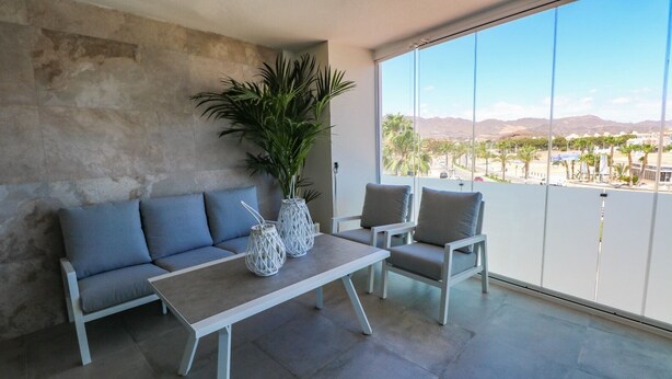 Una sala moderna con un sofá, dos sillones, una mesa de centro y un amplio ventanal con vistas a palmeras y montañas.
