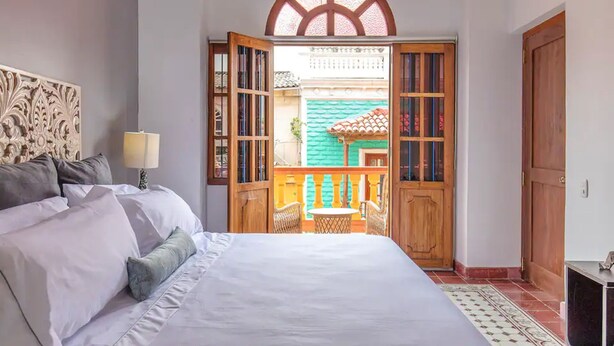 A bedroom with a large bed, a wooden door leading to an outdoor area, and a decorative headboard. - 2CM-B1 APARTAMENTO EN GETSEMANI CON BALC (Cartagena)