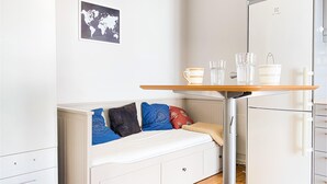 Una piccola cucina componibile con un frigorifero bianco, un tavolino con una tazza e dei bicchieri, e un letto con cuscini a fantasia.