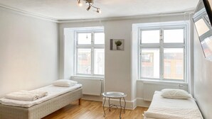 A small, bright room with two single beds, a small table, and large windows with blinds. - Cozy apartment in Visby with kitchen (Visby)