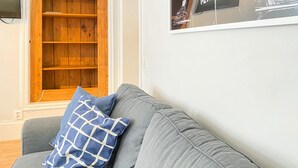 A grey sofa with a blue and white pillow, a wooden shelf unit, and a framed picture on the wall. - Cozy apartment in Visby with kitchen (Visby)