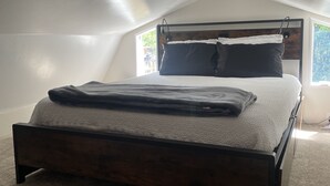 A bedroom with a sloped ceiling, a bed with a wooden frame, a headboard, and a window.