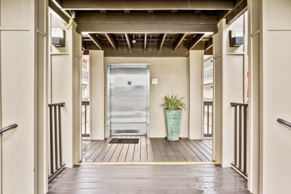 Un acceso cubierto con una puerta metálica, una planta en maceta y una terraza de madera.