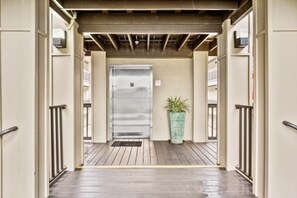 A covered entrance with a metal door, a potted plant, and a wooden deck. - Oceanfront 2BR • Pool • Walk Beach • Sleeps 6 (Fernandina Beach)